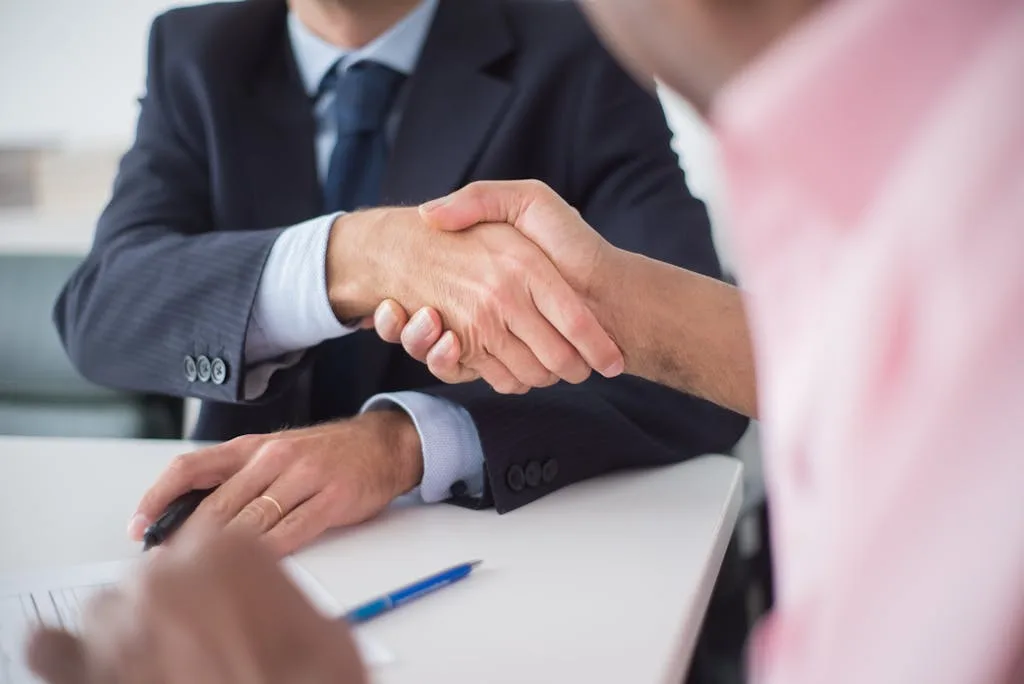 Two businessmen shaking hands across table, symbolizing agreement and partnership in an office environment.